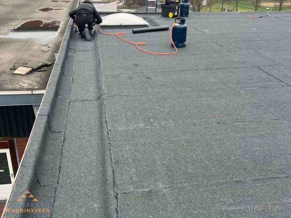 Dakdekker repareert bitumen dakbedekking op groot plat dak in Waddinxveen